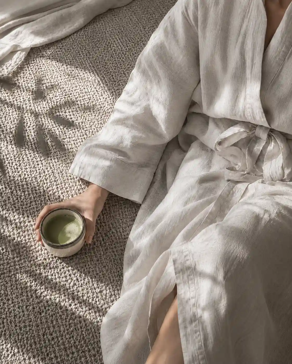 Frau im Leinenmorgenmantel hält eine Schale Matcha-Tee — ruhiger Morgen nach gutem Schlaf